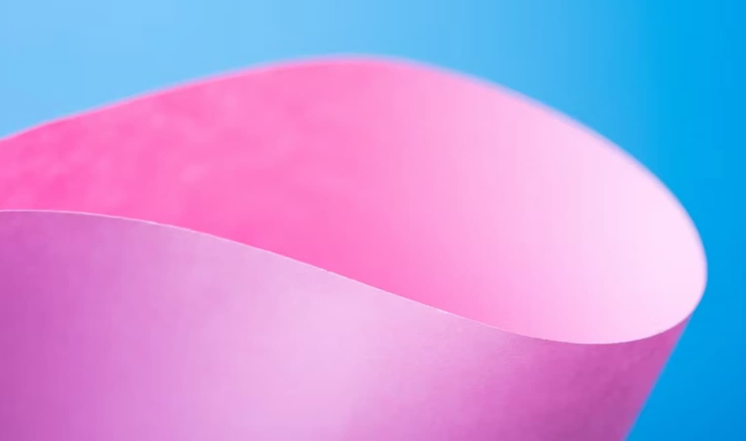 A bright pink sheet of paper curves in front of a rich blue background.